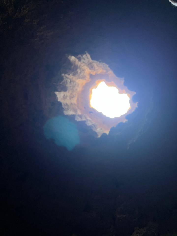 Looking up through irregular cave opening to bright sky above.