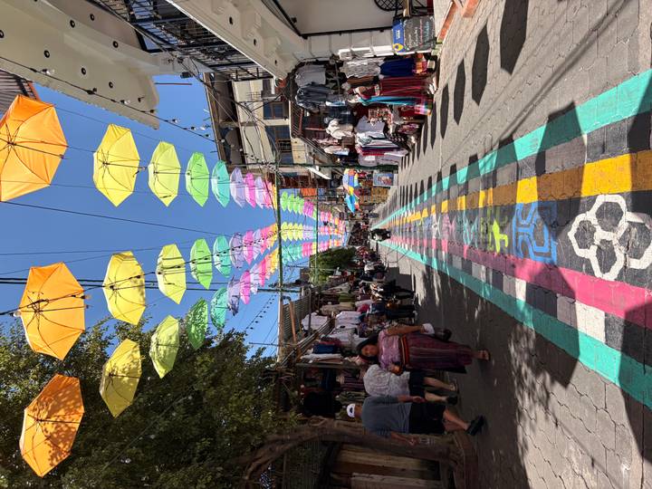 Bustling market street under a canopy of bright umbrellas and multicolored painted walkway.