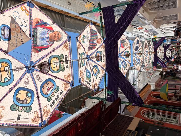 Street scene with large patterned sunshades depicting Mayan symbols and portraits suspended over shoppers.