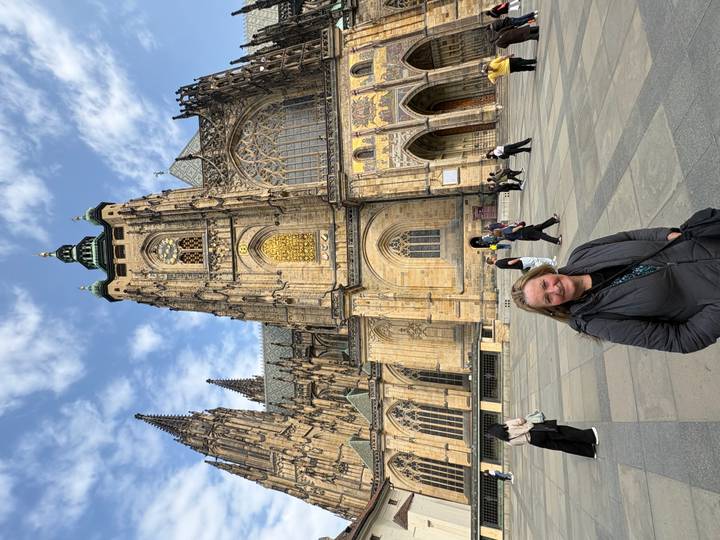 Smiling traveler standing in front of the gothic façade of St. Vitus Cathedral within Prague Castle complex.