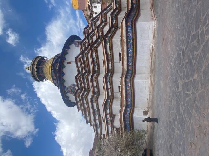 Tiered Gyantse Kumbum stupa with vibrant mural bands under a blue sky on the Tibetan Plateau.