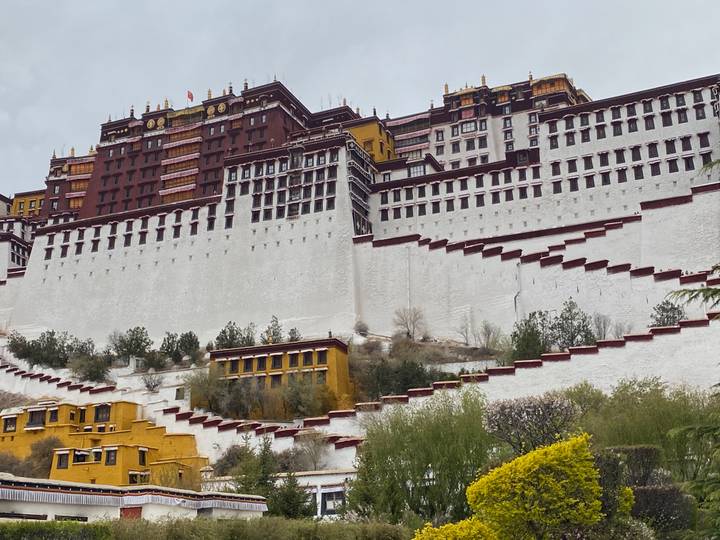 Potala Palace’s massive white and ochre walls cascade down the hillside under a cloudy Tibetan sky.