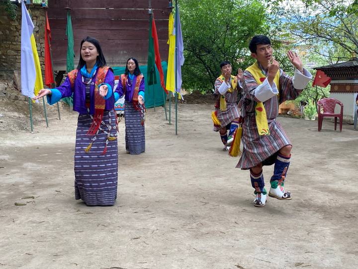 Bhutanese dancers in colorful traditional dress perform an outdoor folk dance with joyous expressions.