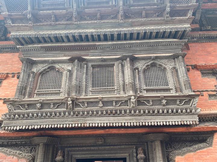 Close-up of intricately carved wooden window frame on a historic Newari brick building in Kathmandu.