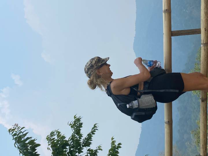 Female hiker with backpack pauses for water against a hazy mountain backdrop.