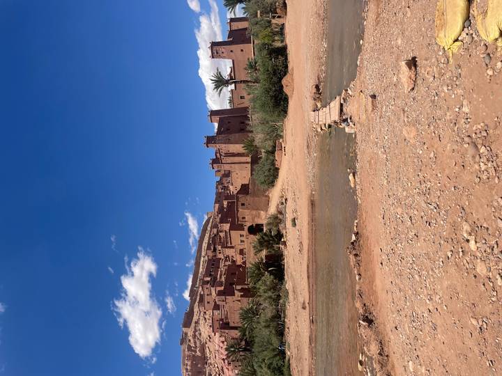 Clay-brick kasbah of Ait Benhaddou framed by blue sky with a shallow river in front.