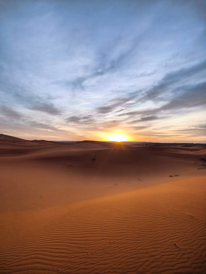 Golden sun setting over rolling orange Sahara sand dunes under a colorful sky