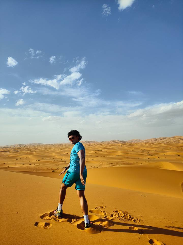 Traveler in blue shirt standing on ridge overlooking endless ochre sand sea