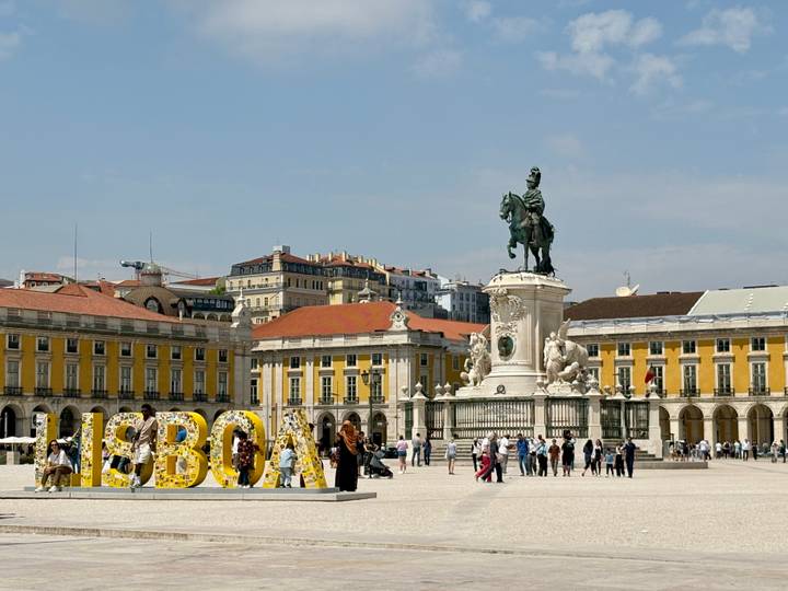 Praça do Comércio in Lisbon with the equestrian statue of King José I and yellow arcaded buildings under a blue sky.