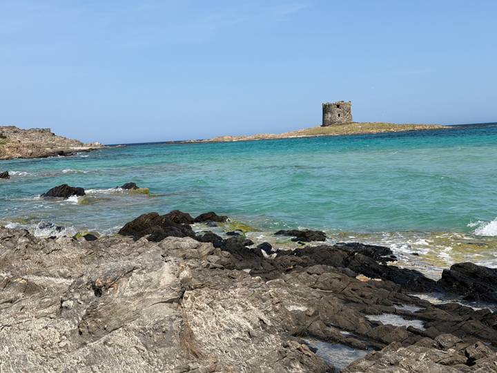 Turquoise waters lap against rocky shorelines with an old stone watchtower on a small island off Stintino.