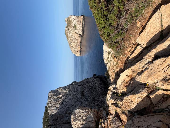 Sheer limestone cliffs framing a calm blue cove under a clear sky on Sardinia’s coast.
