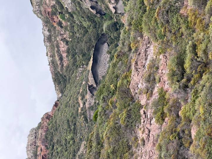 Unusual concave rock shelter nestled in rugged green hills after rainfall.