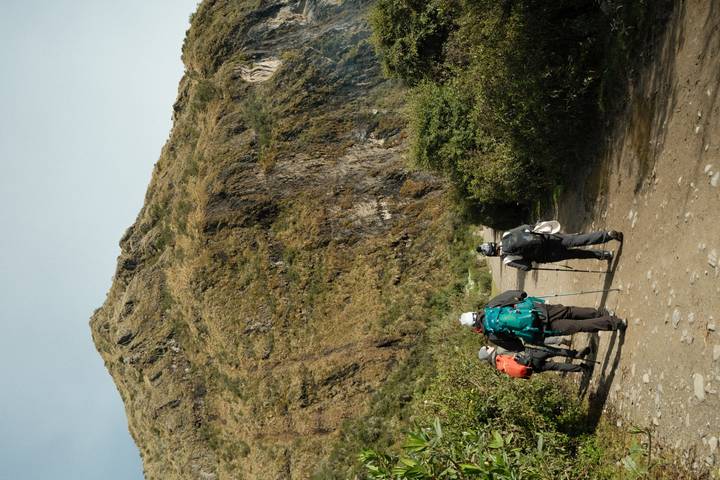 Back view of trekkers with backpacks and walking poles heading up a rugged Andean trail.