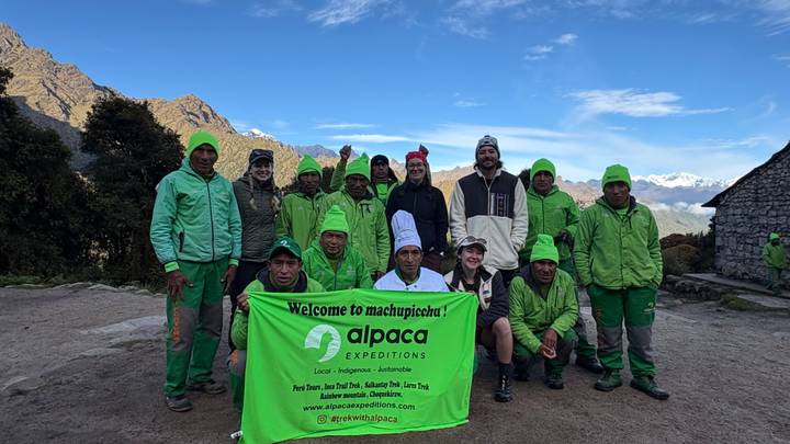 Team of guides and porters in green jackets pose with an Alpaca Expeditions banner on the trail to Machu Picchu.