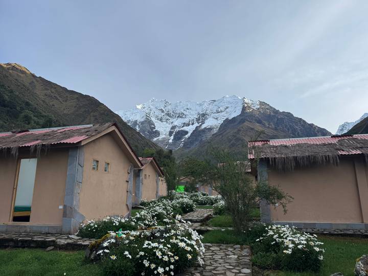 Mountain lodge huts surrounded by white flowers with a glacier-topped peak behind.