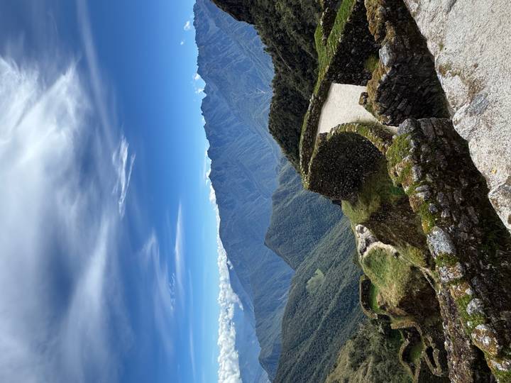 Stone Inca ruins perched on a ridge with sweeping views of green Andes under a striking sky.
