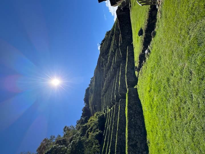 Sunburst over ancient agricultural terraces covered in green grass.