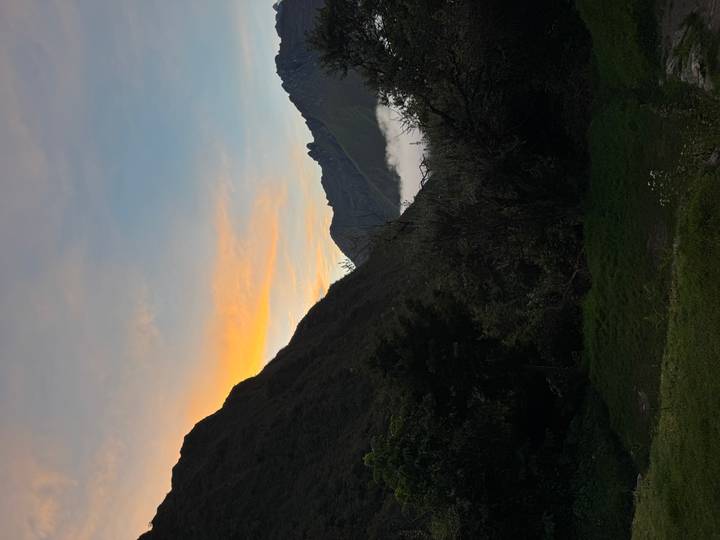 Soft sunset glow behind rugged mountain silhouettes and low valley cloud.