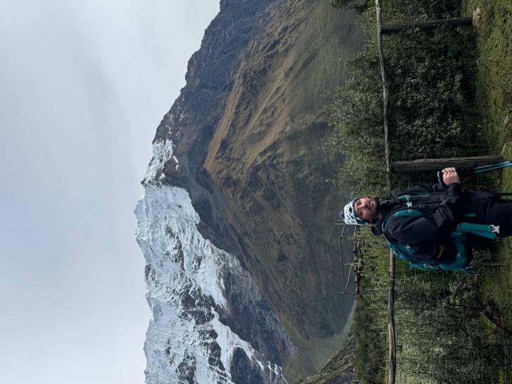 Trekkker posing with towering glacier-clad mountain backdrop.