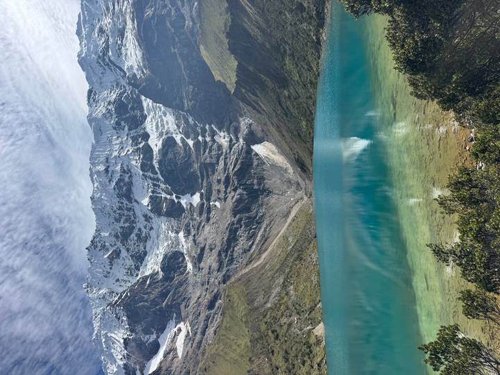 Turquoise alpine lake mirroring dramatic glacier wall beneath patterned sky.