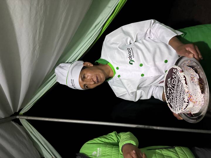 Camp chef in uniform presenting a decorated cake inside a dining tent.
