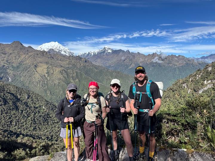 Four hikers posing on ridge with panoramic view of snow-topped Andes.