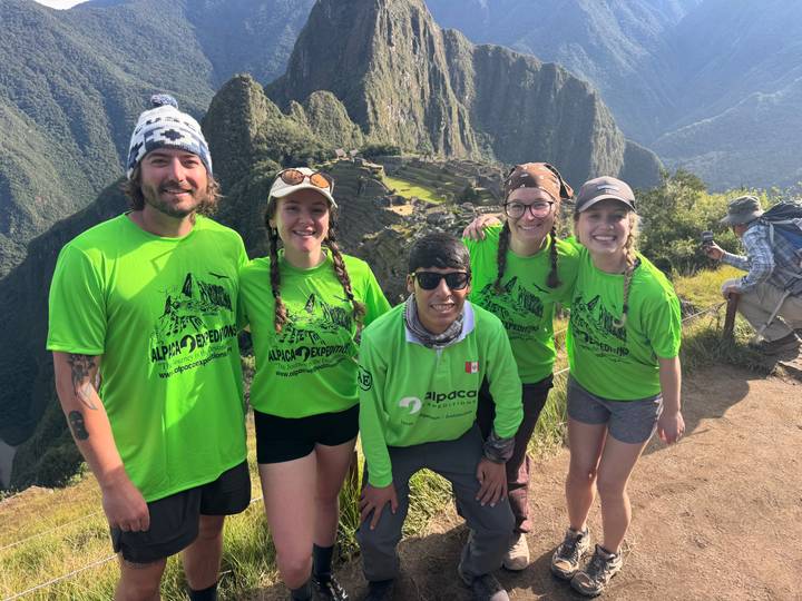 Trekkers wearing matching green shirts smiling in front of Machu Picchu viewpoint.