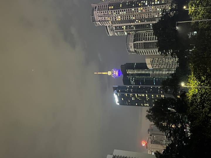 Night view of Kuala Lumpur skyline featuring illuminated KL Tower against cloudy sky.
