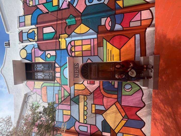 Vibrant mural-covered building facade with two travellers sitting on the entrance steps.