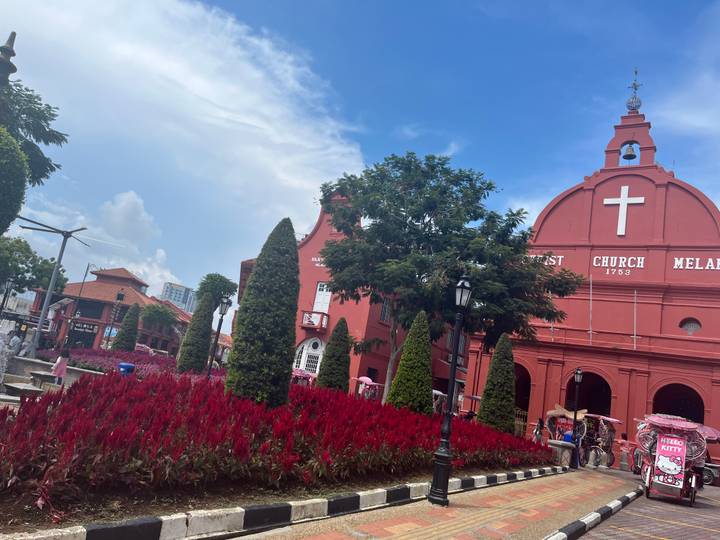 Historic red Christ Church Melaka framed by gardens under a bright sky.