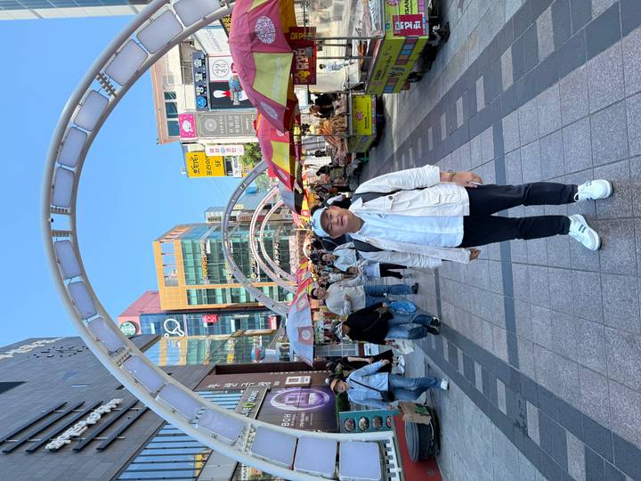 Traveler posing in a bustling Korean street market lined with colorful stalls and arching overhead structures.