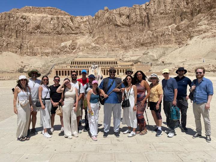 Tour group posing in front of the monumental Temple of Hatshepsut carved into the desert cliffs.