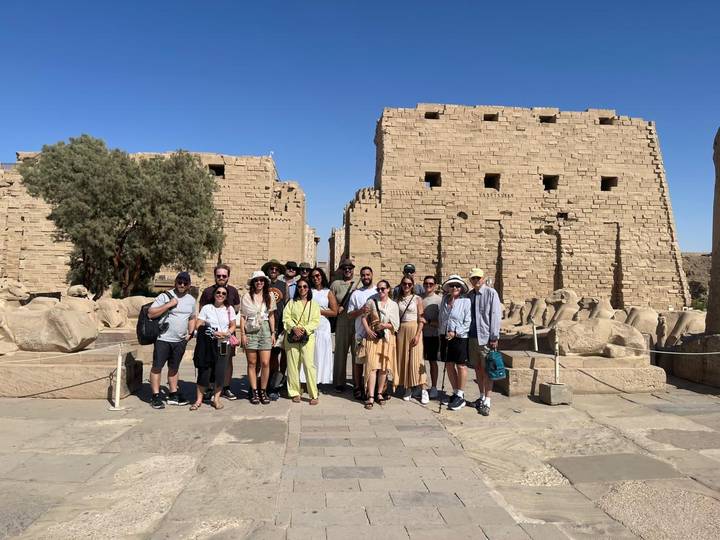 Tour group assembled inside Karnak Temple complex with towering sandstone walls and statues behind them.
