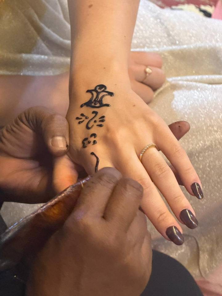 Close-up of henna artist applying black ink Egyptian symbols to a traveler’s hand.