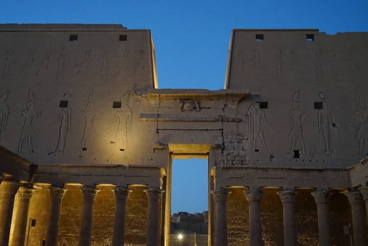 Nighttime illumination highlighting hieroglyph‐covered pylons and columns of an ancient Egyptian temple.