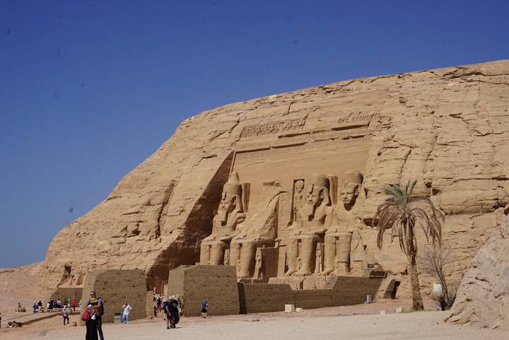 The great rock-cut façade of Abu Simbel with colossal seated statues under a clear blue sky.