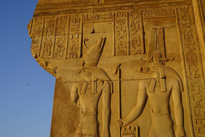 Golden side-lit close-up of intricate hieroglyphic reliefs on an ancient sandstone wall.