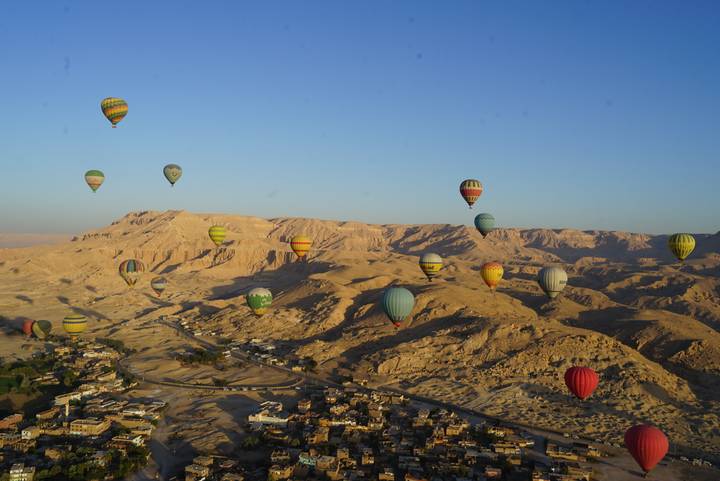 Dozens of colorful hot-air balloons drifting over the rugged desert mountains of Luxor at sunrise.