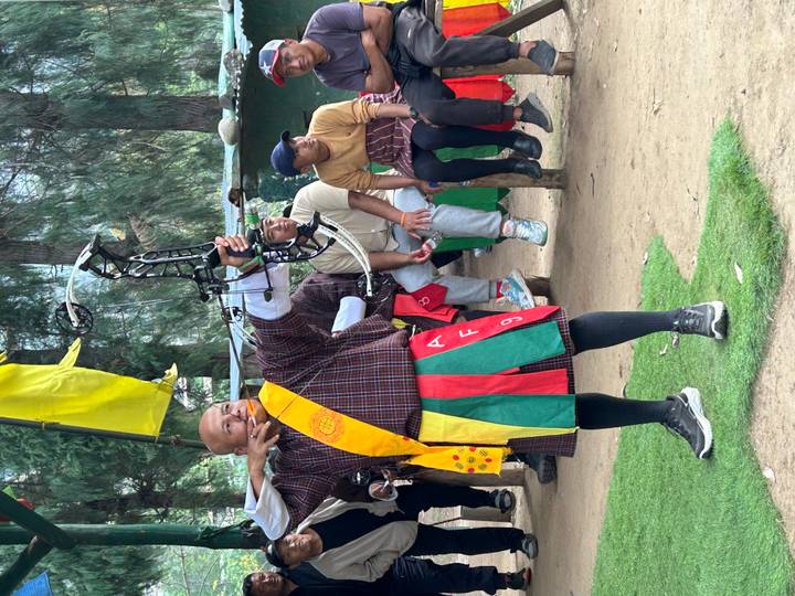 Bhutanese archer aiming a modern bow while spectators watch at an outdoor range.
