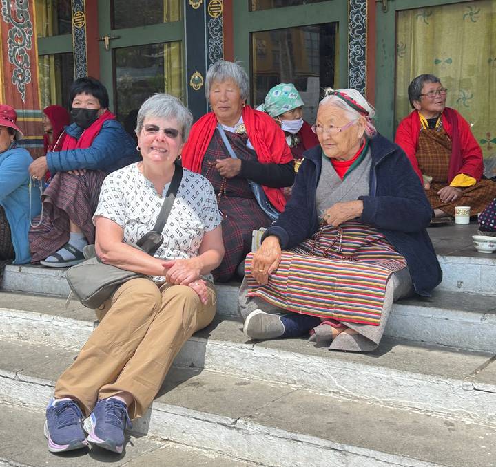 Tourist seated on temple steps chatting with elderly local women in colorful attire.