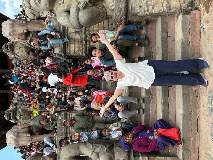 Large crowd gathered on stone temple steps with one traveler posing joyfully in front.
