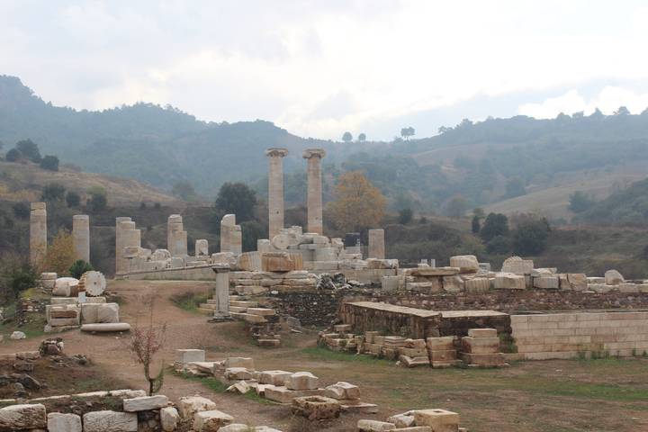 Ruined stone columns and scattered blocks of an ancient Anatolian archaeological site under overcast skies.