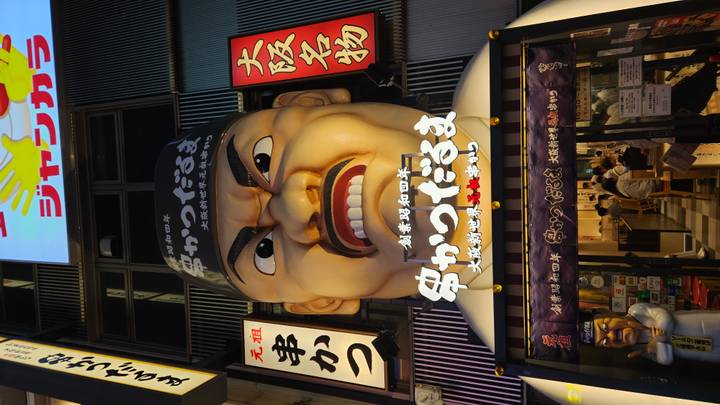 A flamboyant restaurant facade in Osaka features an enormous 3-D caricature face surrounded by bright signage.