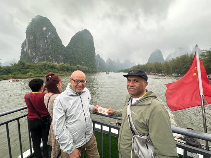Tourists on a river boat pose with a Chinese banknote against the dramatic karst peaks of the Li River.