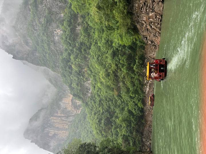 Small red tourist boats navigating a misty green gorge surrounded by towering cliffs