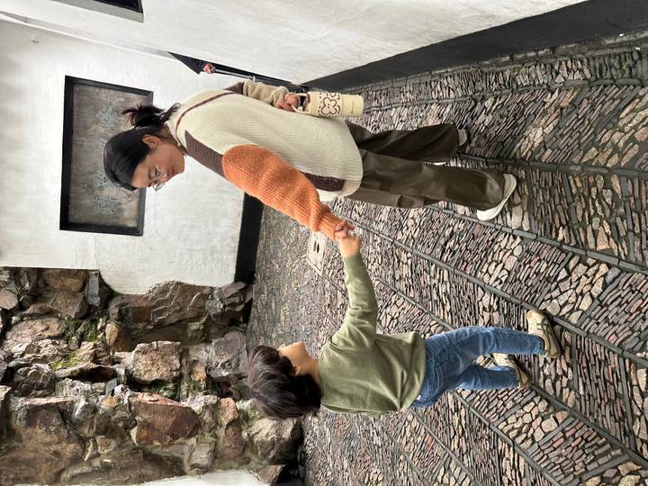 Woman holding a young child’s hand while walking along a cobblestone pathway near rock walls