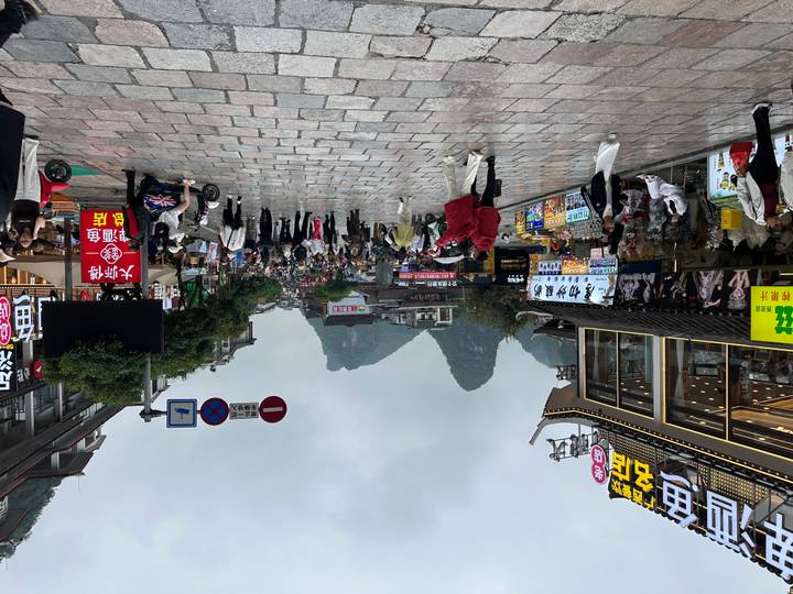 Busy pedestrian street lined with shops and neon signs set against misty karst mountains