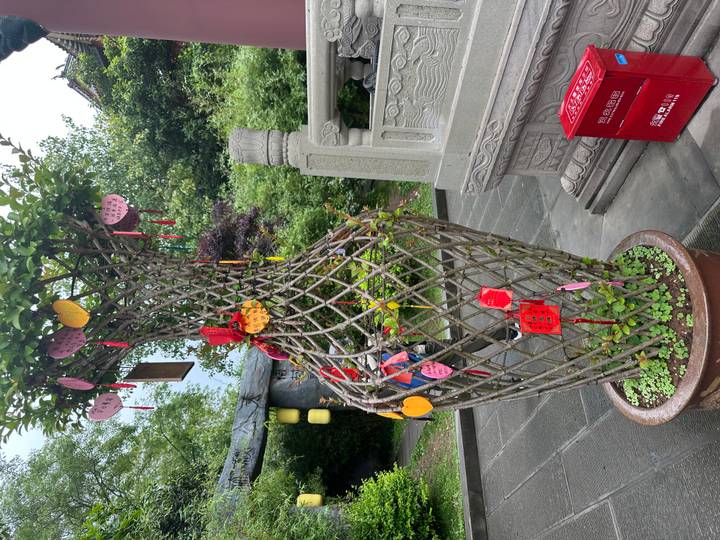 Decorative lattice tree planter festooned with red and yellow hanging wishes beside carved stone railing