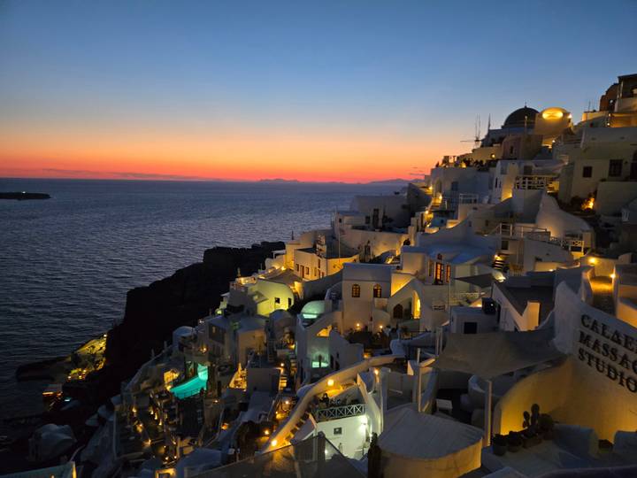 Iconic village of Oia illuminated at dusk with white houses and blue domes cascading down the cliff.