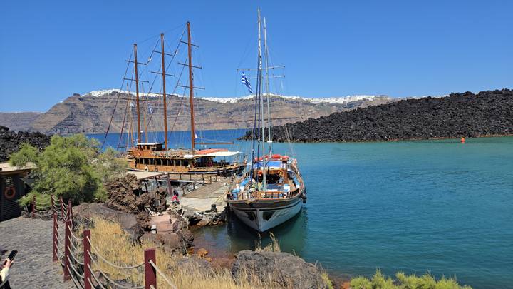 Wooden sailing ship moored in turquoise volcanic bay with black lava rocks behind.